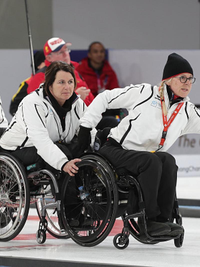 a female wheelchair curler pushes the stone across the ice