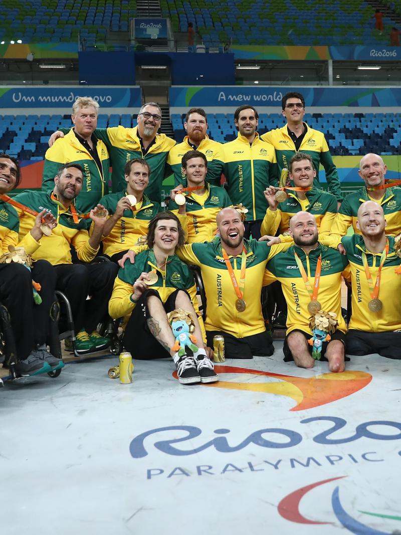 a group of wheelchair rugby players pose on the court with their medals