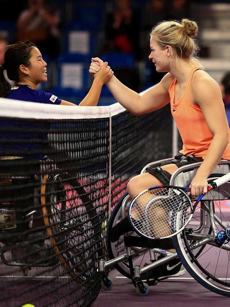 two female wheelchair tennis players shake hands over the net