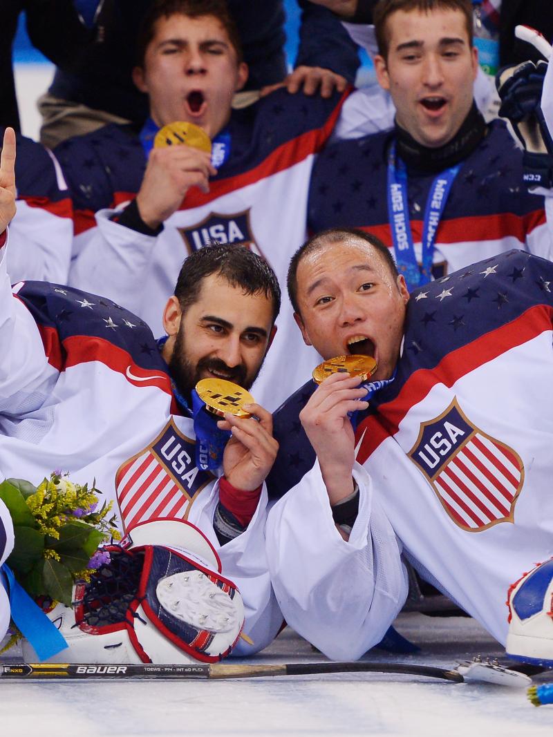a group of male para ice hockey players lie on the ice and bite their medals in celebration