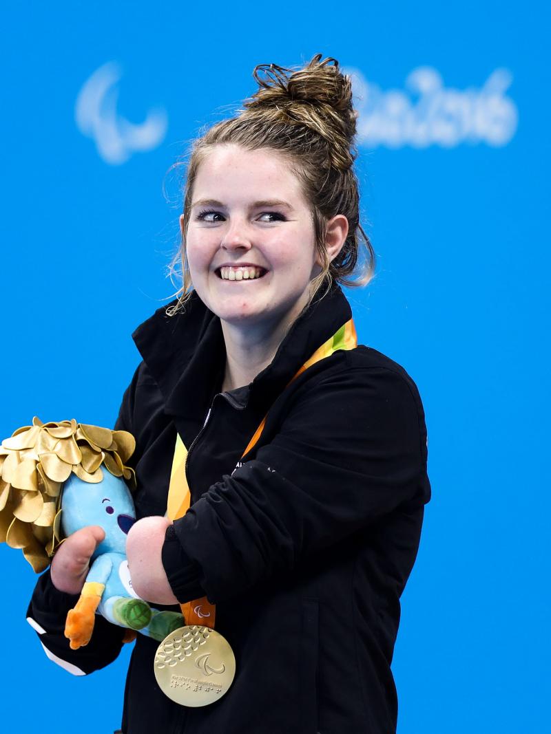 a Para swimmer smiles with her gold medal on the podium