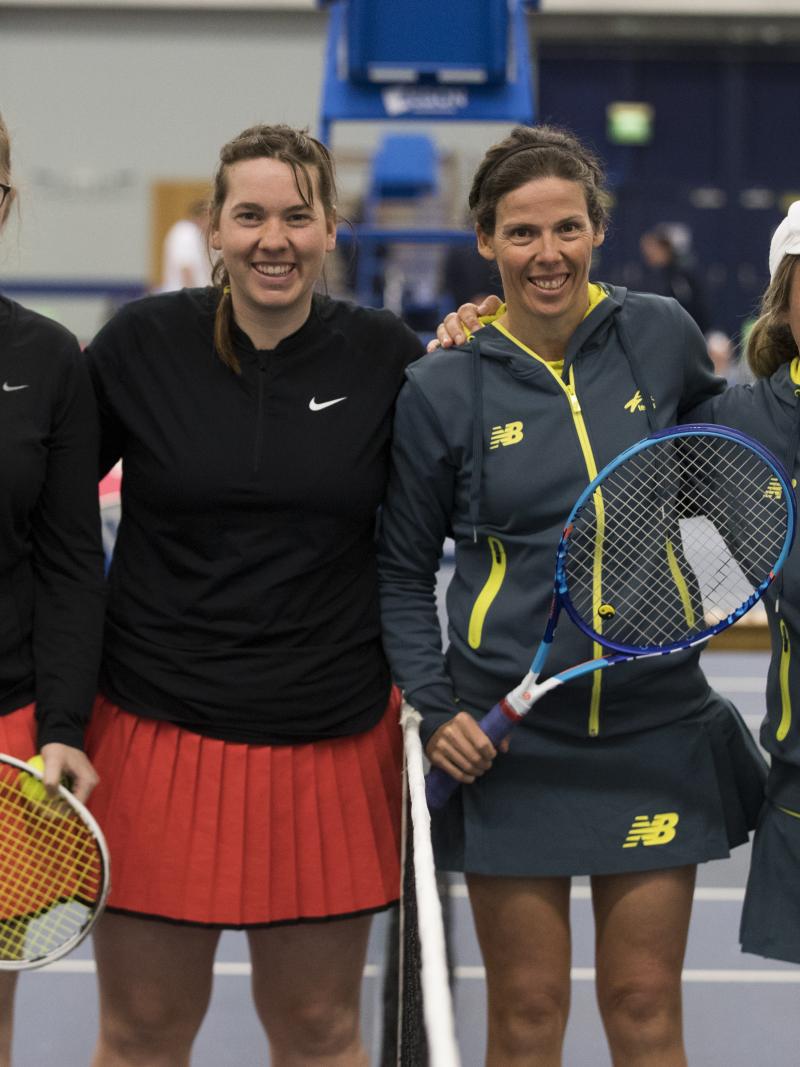 four female tennis players stand at the net