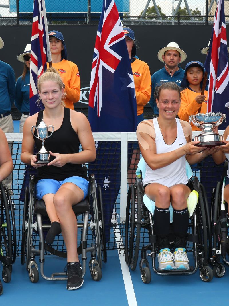 four female wheelchair tennis players hold up their trophies on court
