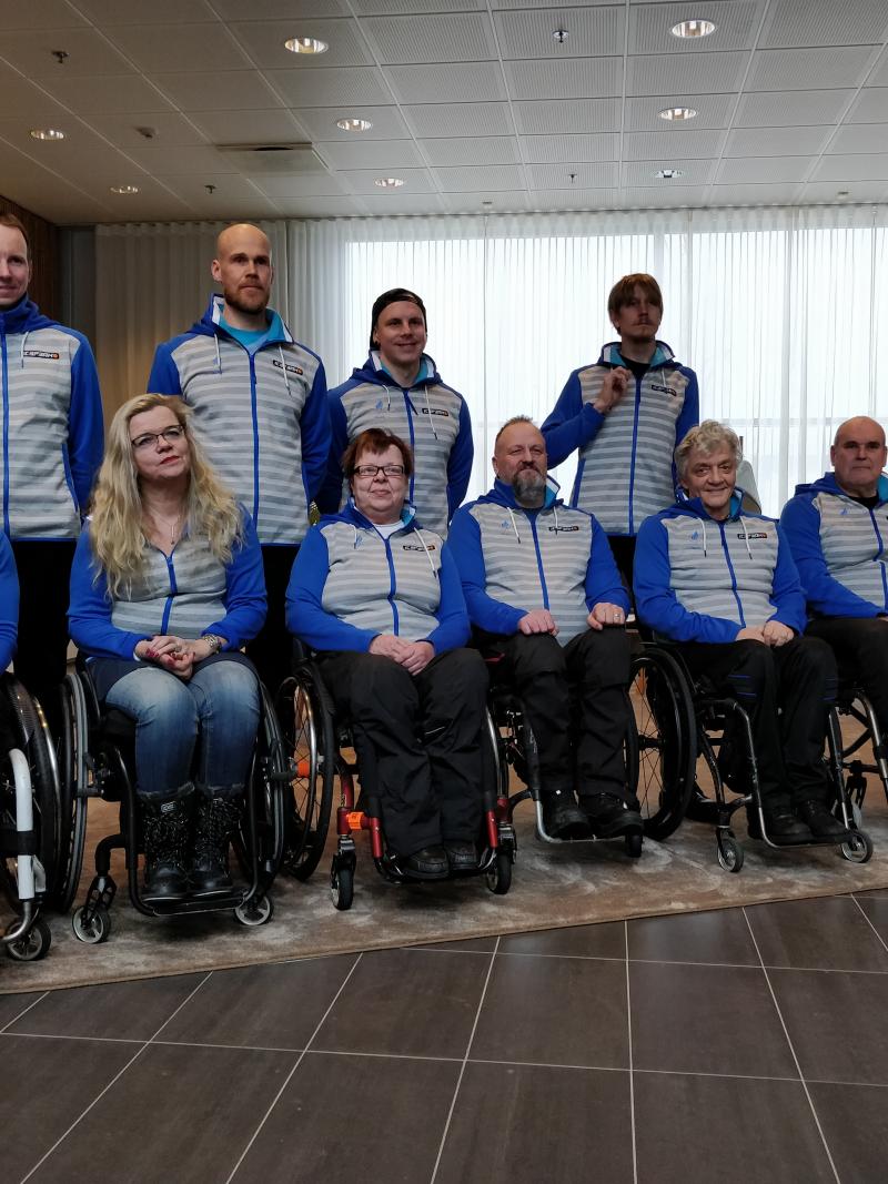 Four people standing behind a group of six people in wheelchairs