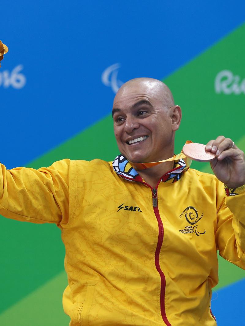 a male Para swimmer holds his bronze medal aloft