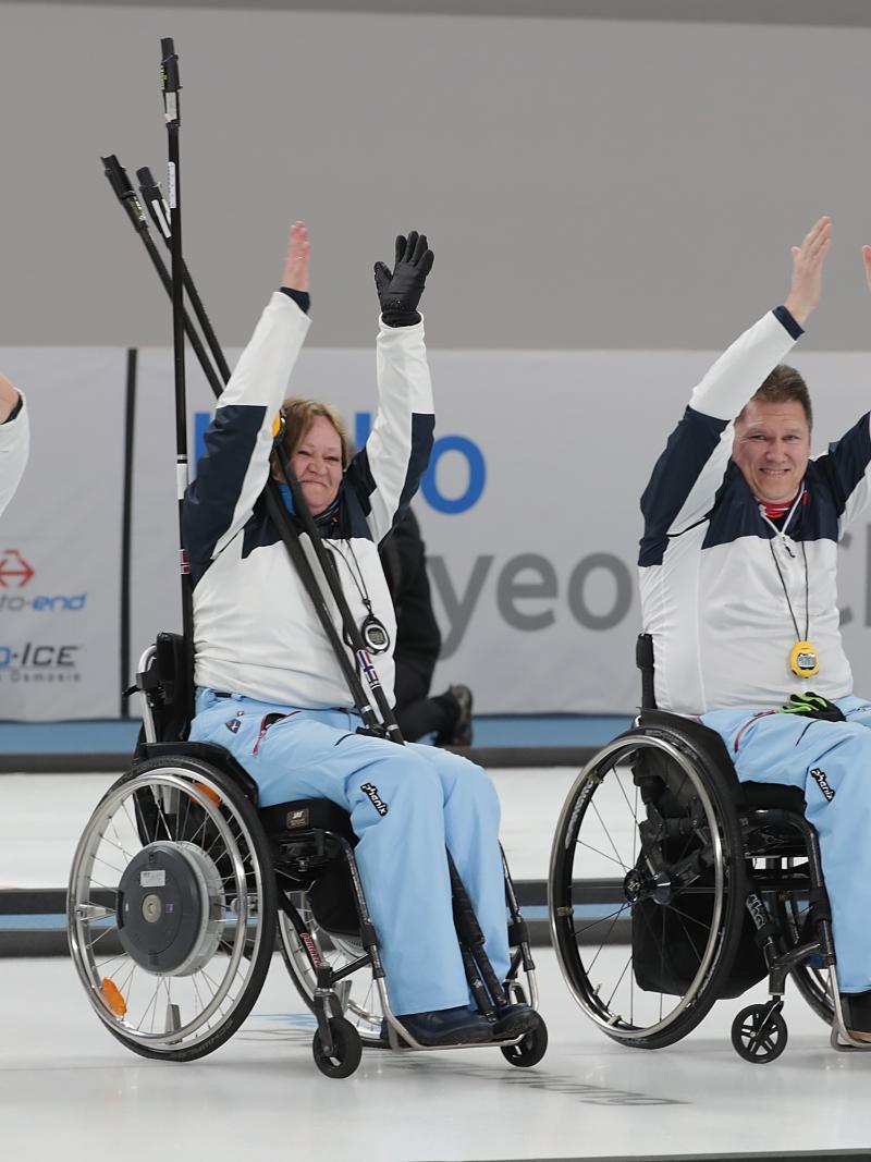 four wheelchair curlers raise their arms in celebration