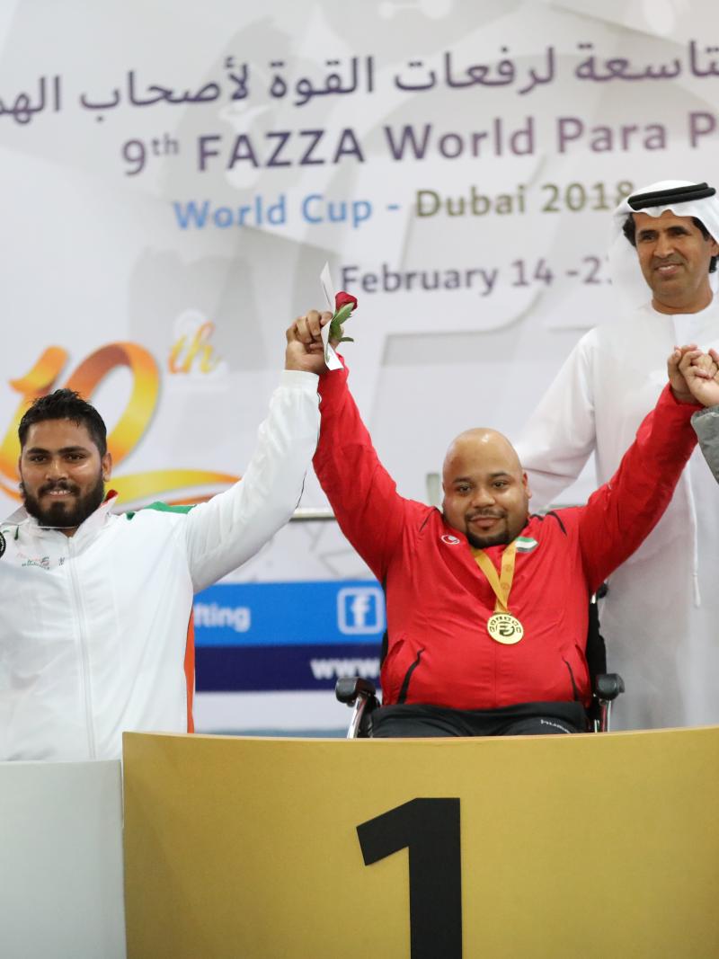 three male powerlifters raise their arms on the podium