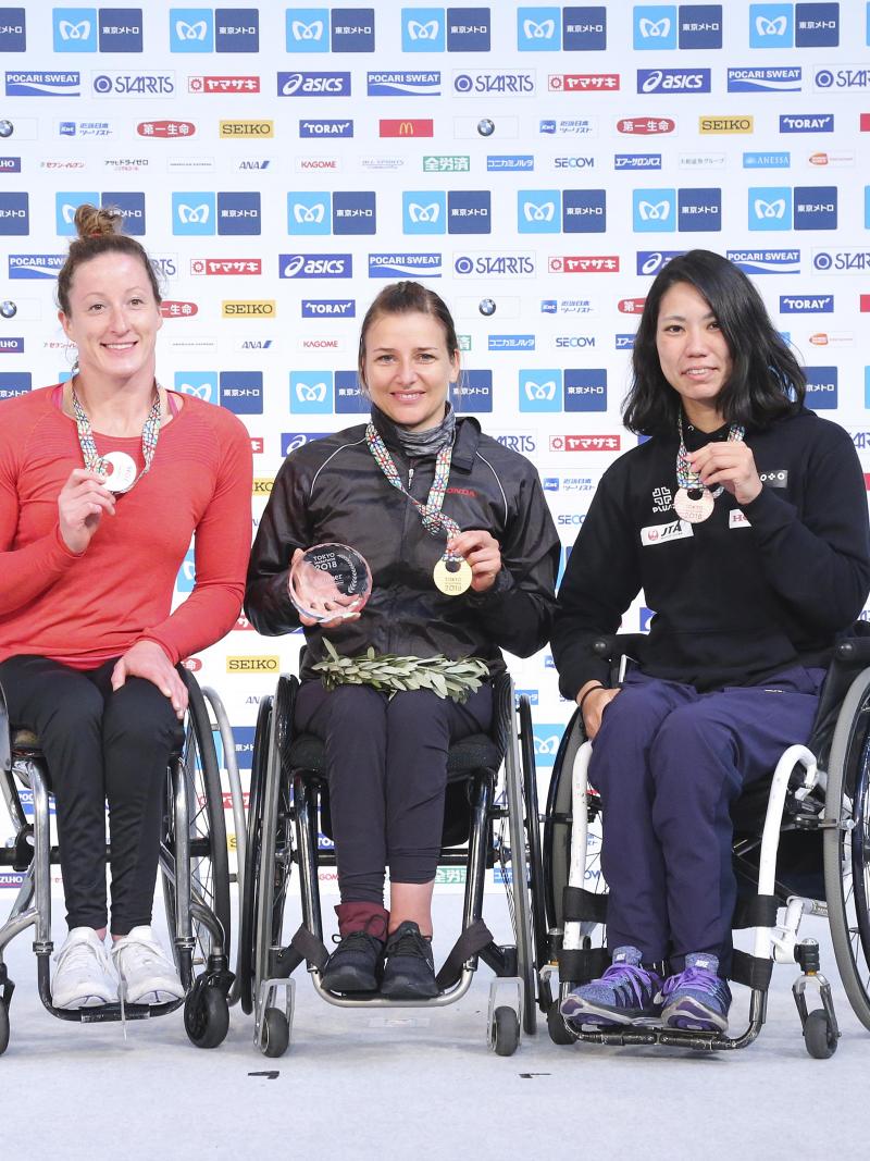 three female wheelchair racers on the podium with their medals
