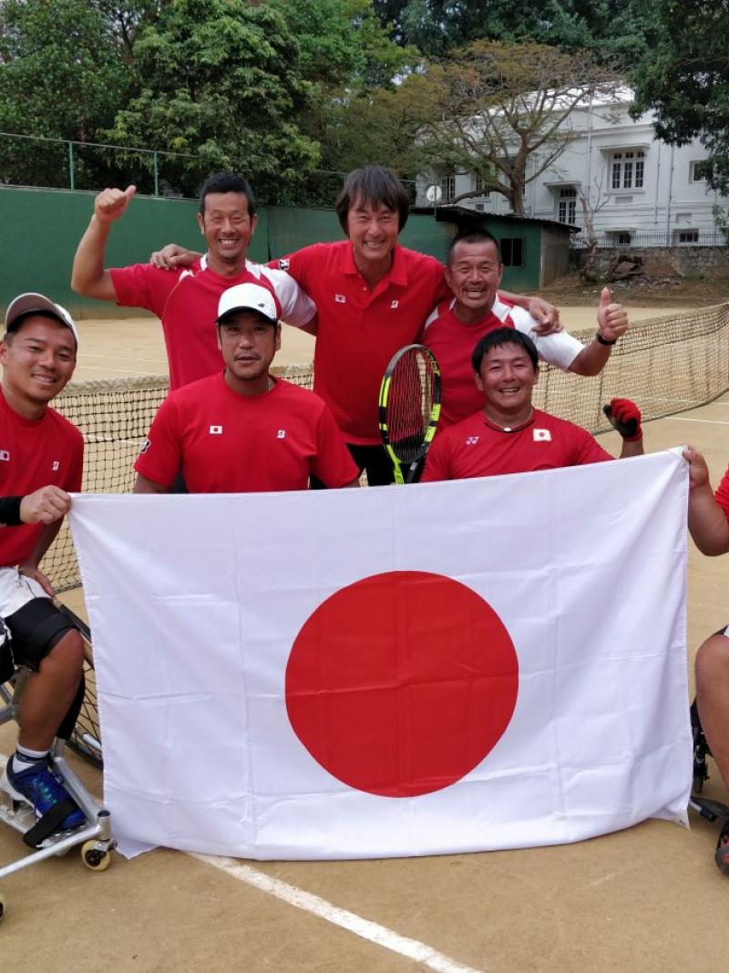 a group of male wheelchair tennis players pose with a Japanese flag