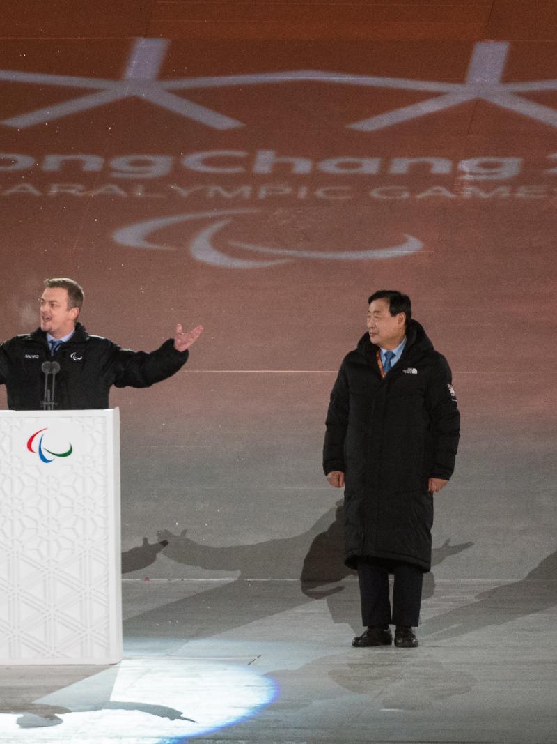 a man spreads his arms wide while speaking at a podium