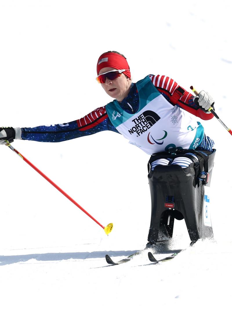 a female sit skier pushes through on the biathlon course