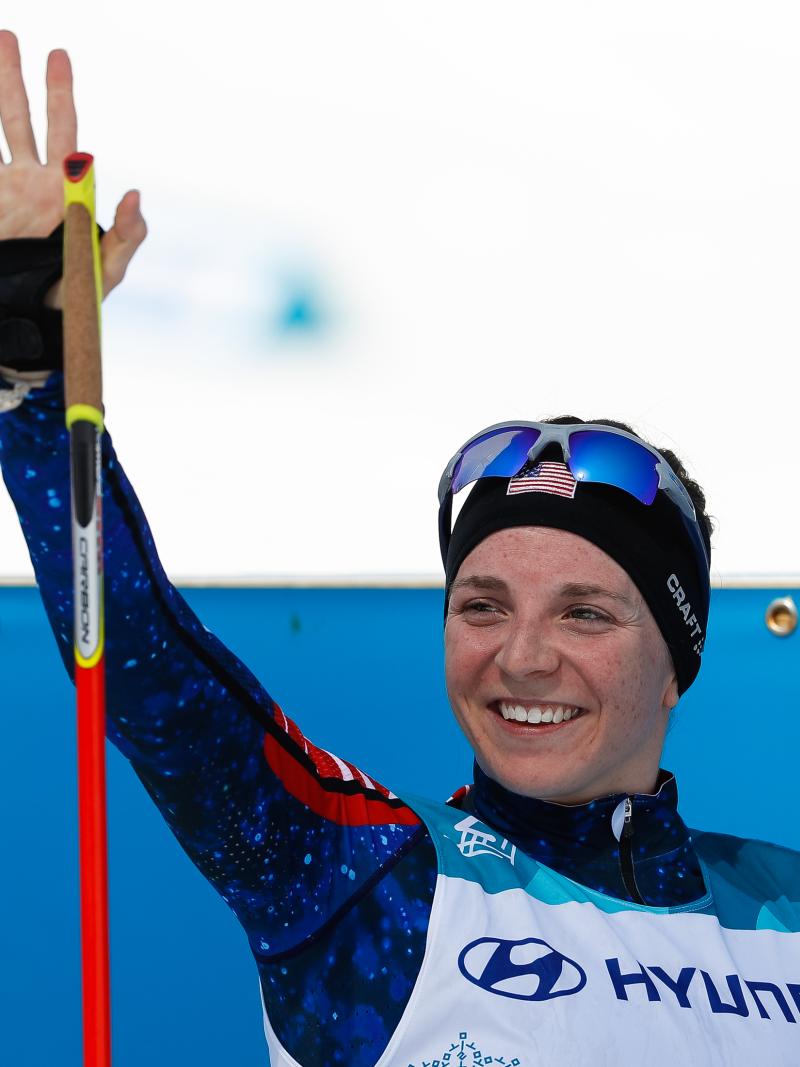 a female Nordic skier smiles and waves