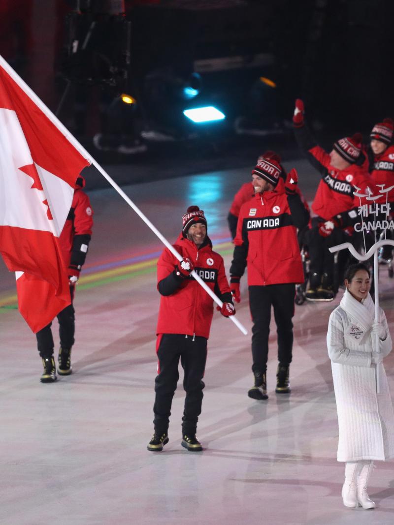 a male Para athlete carrying the Canadian flag