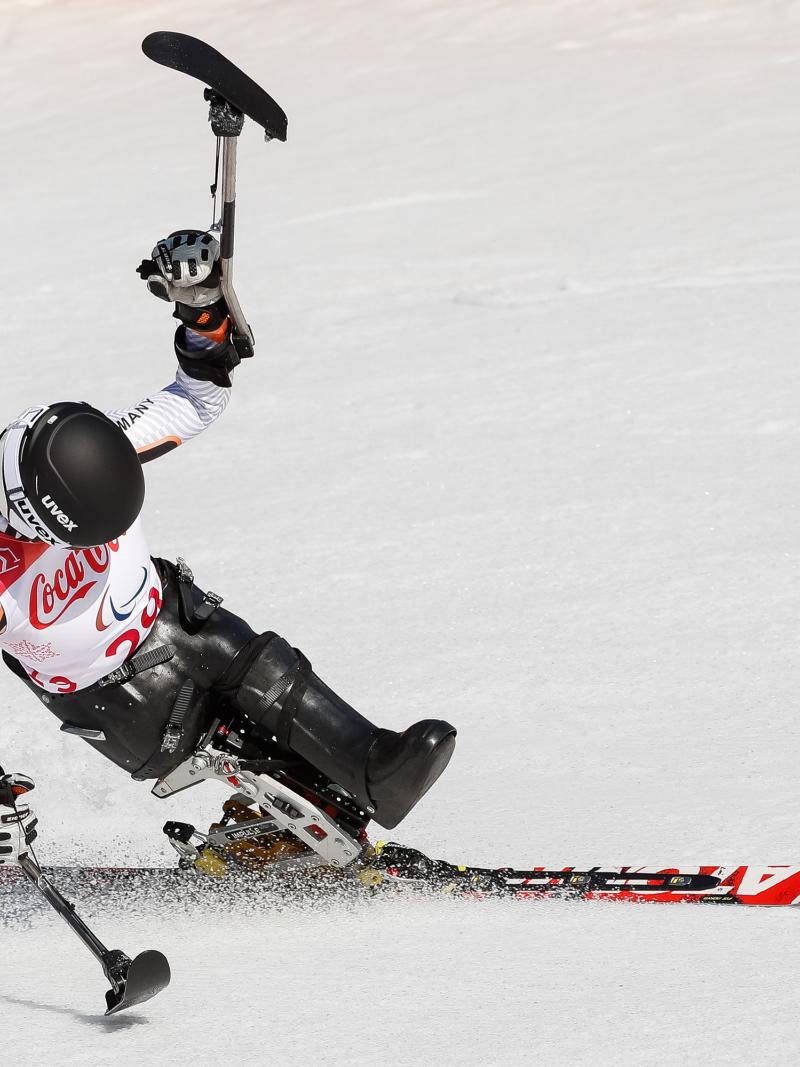 a female sit skier celebrates with her ski in the air