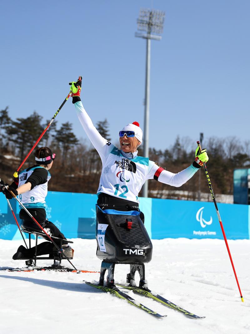 a female Nordic sit skier celebrates on the finish line