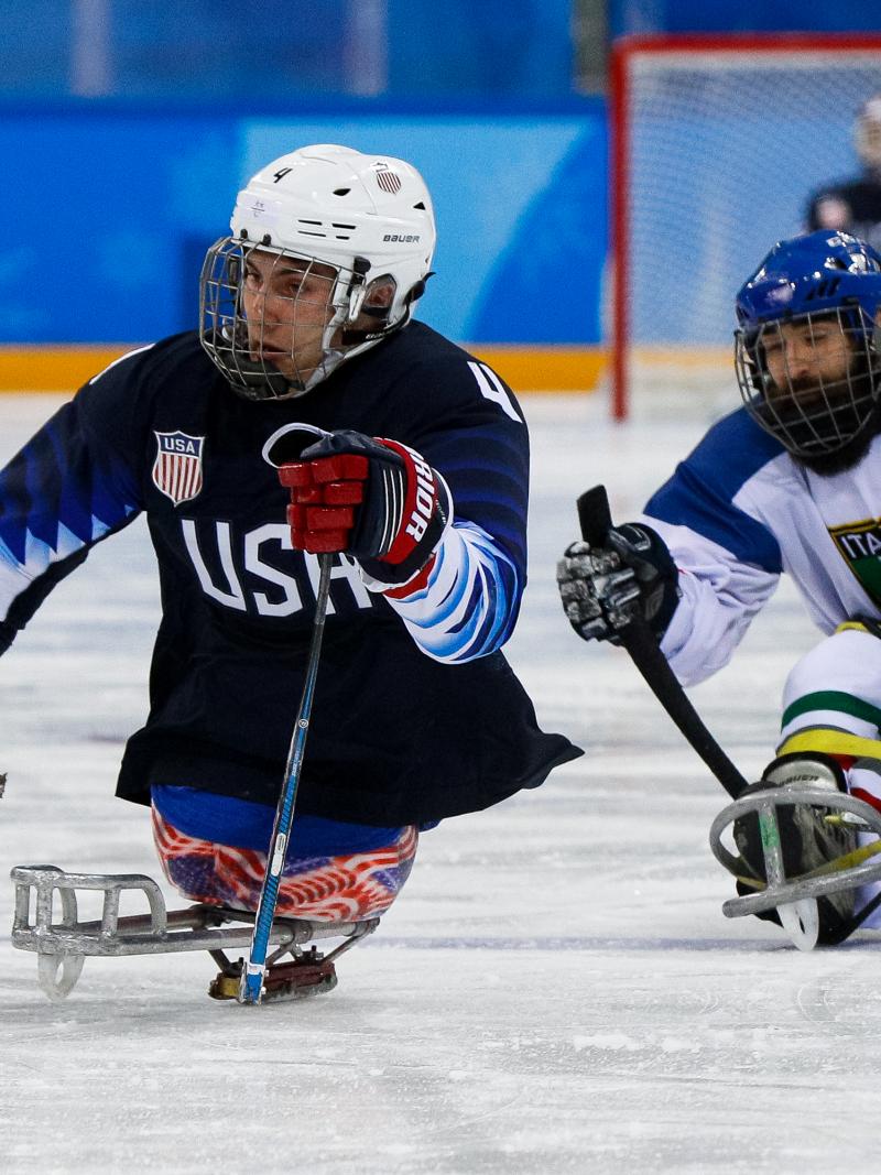 Two athletes on sledges playing Para ice hockey