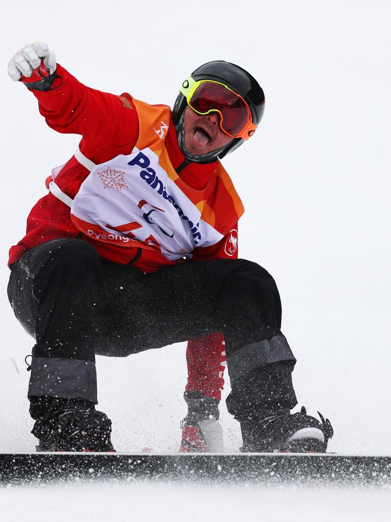 a male Para snowboarder sticks out his tongue at the end of his run