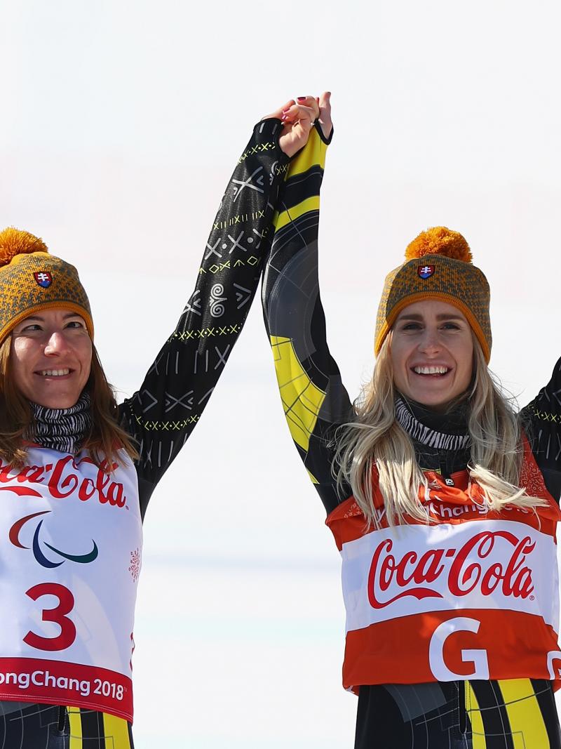 a female vision impaired skier and her guide raise their arms in celebration