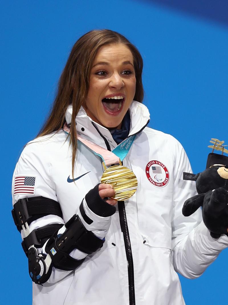 a female Para athlete holds up her gold medal and her mascot
