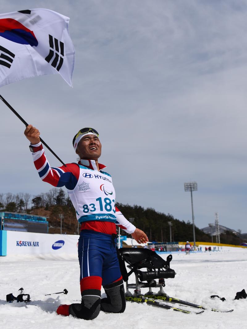 a male Para Nordic skier celebrates with the South Korean flag