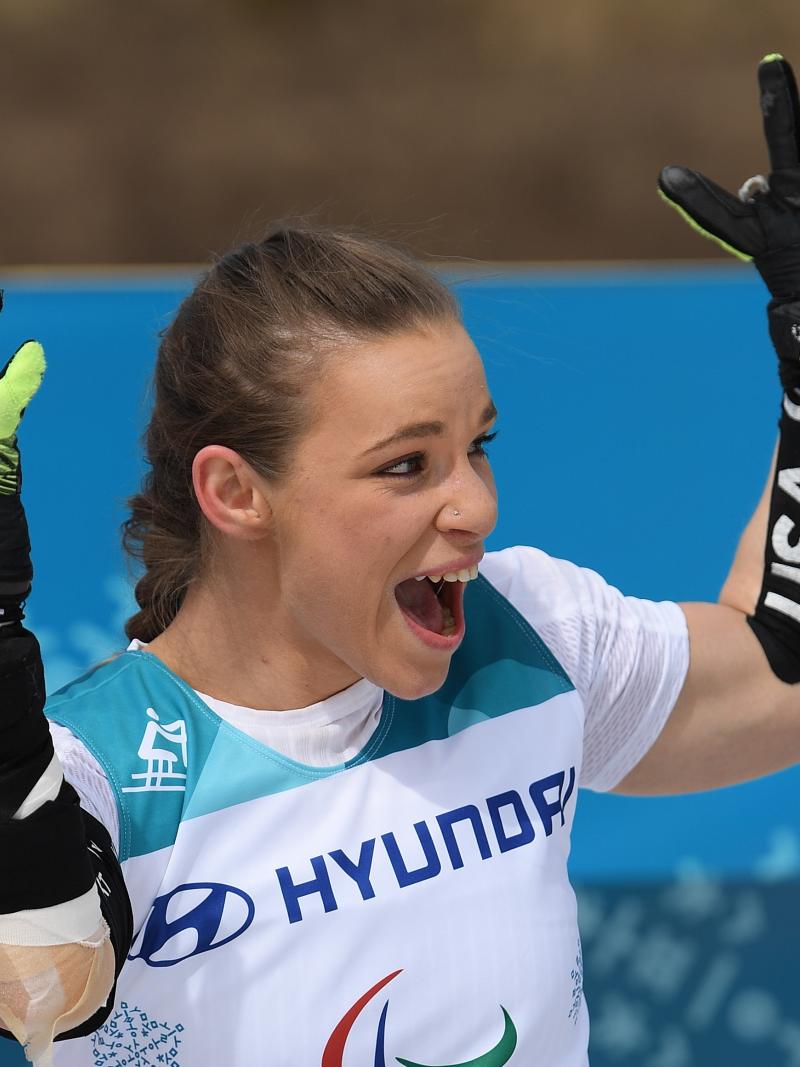 a female sit skier throws up her arms in celebration