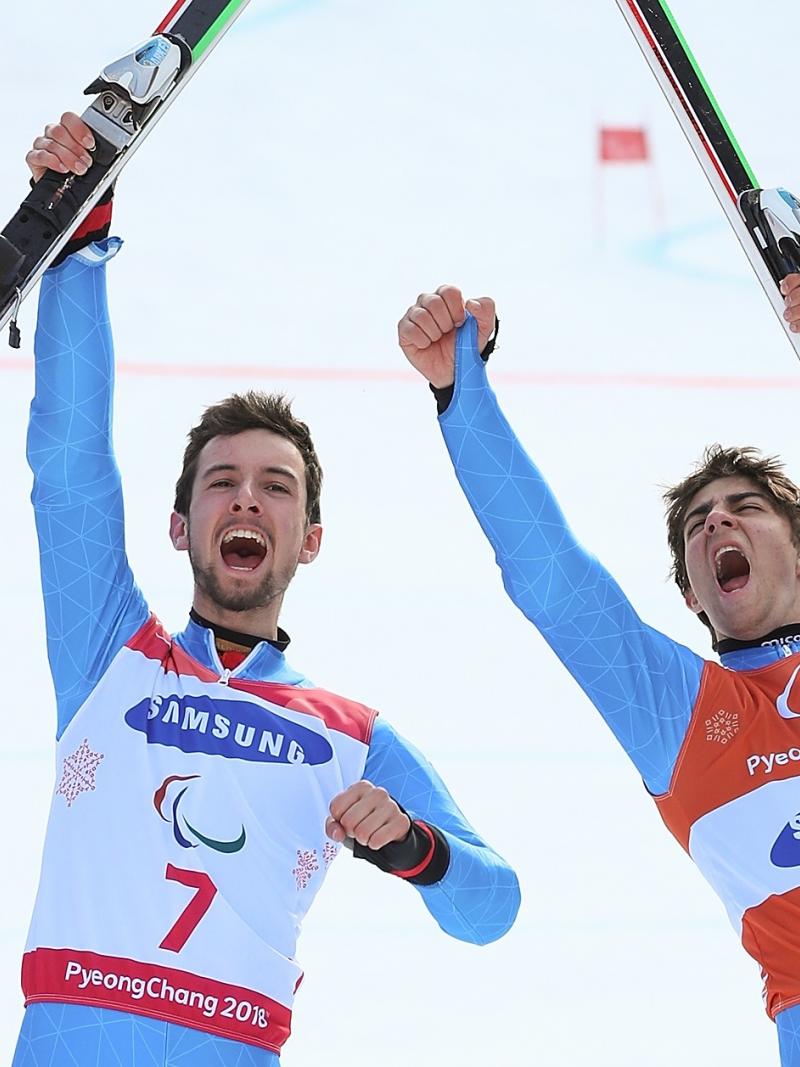 a male vision impaired skier and his guide celebrate by holding up their skis