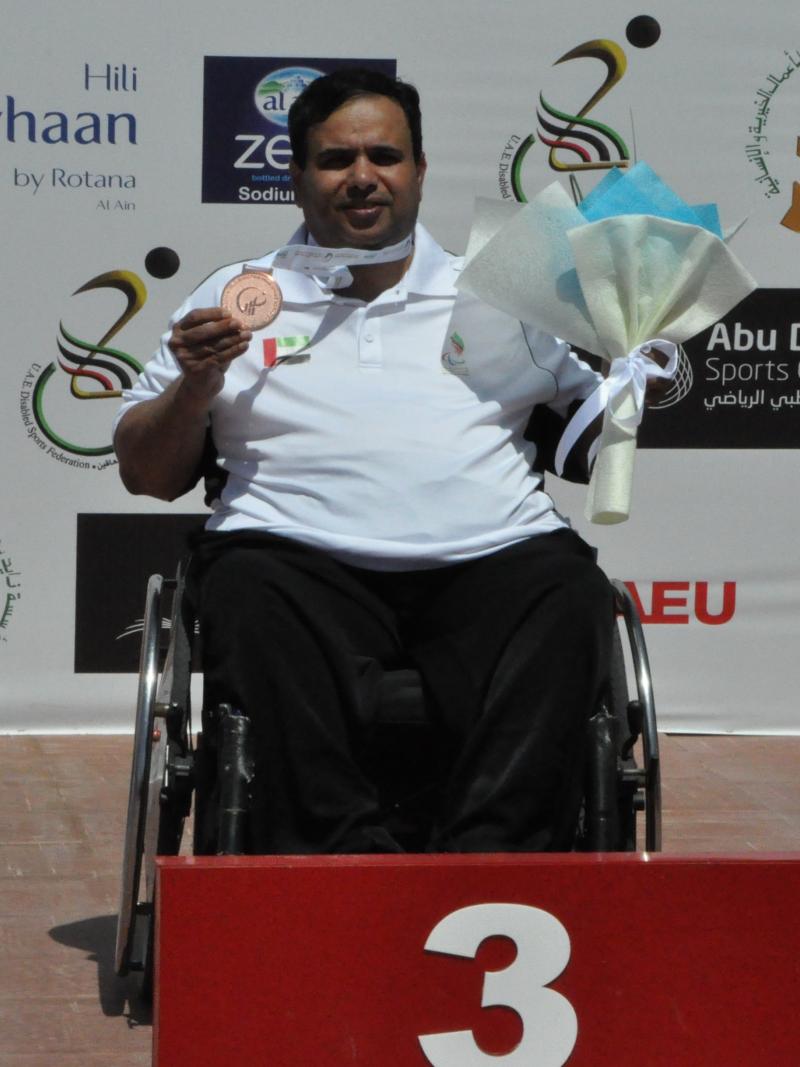 Man in wheelchair holding medal and flowers