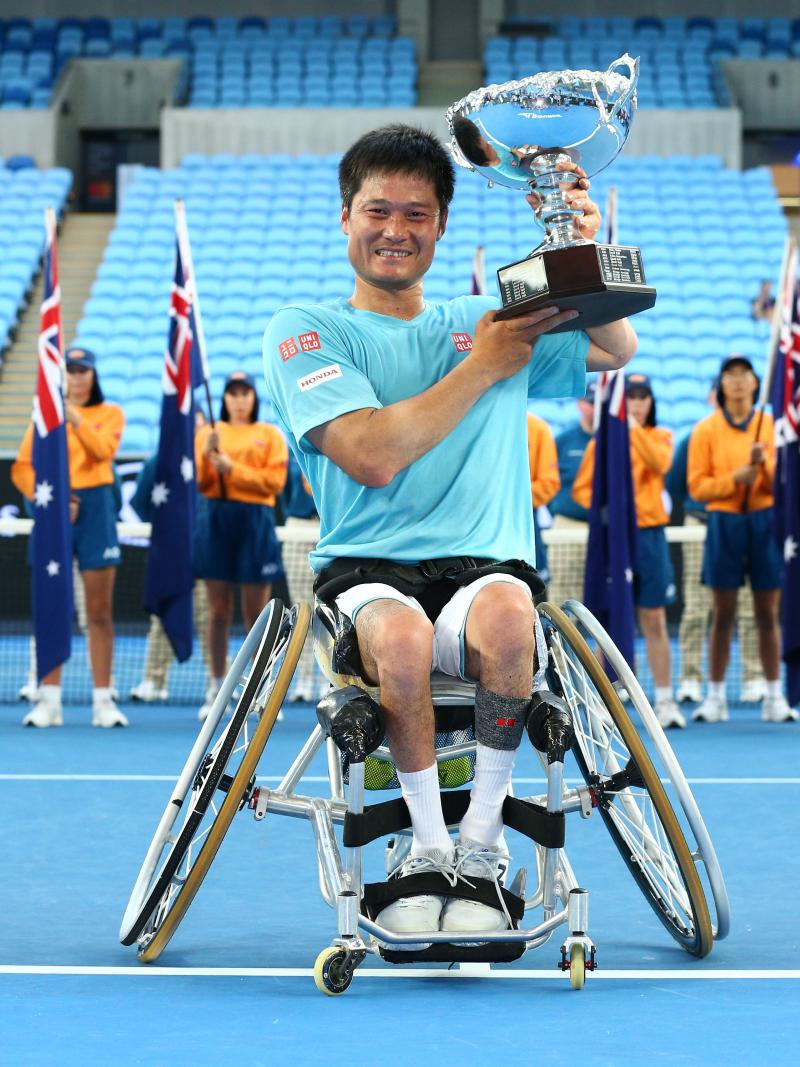 a male wheelchair tennis player lifts a trophy