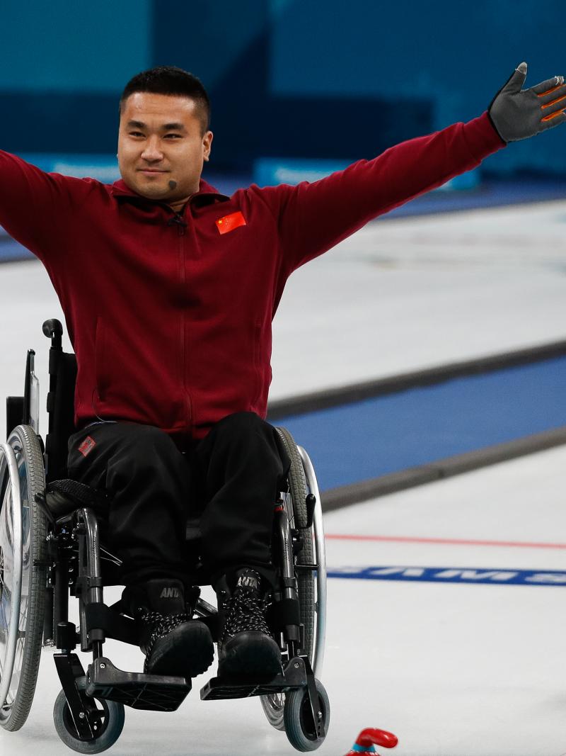 a male wheelchair curler raises his arms in celebration