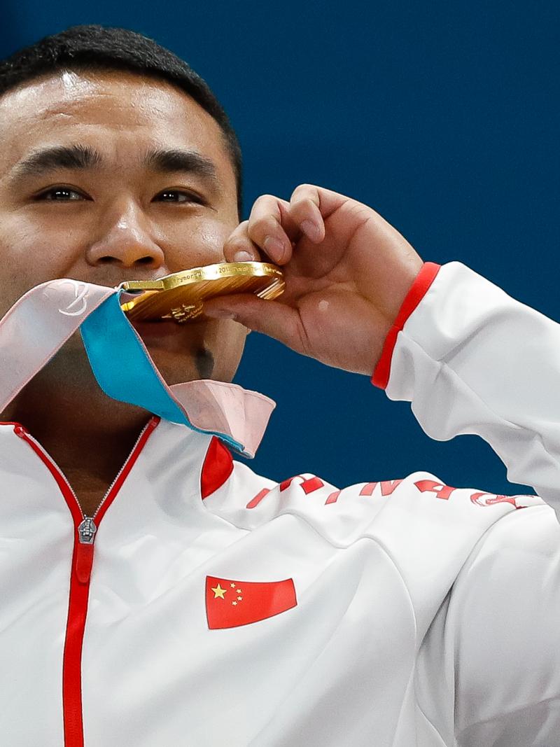 a male curler bites his gold medal