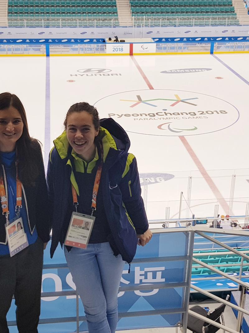two women stand looking down at an ice hockey rink