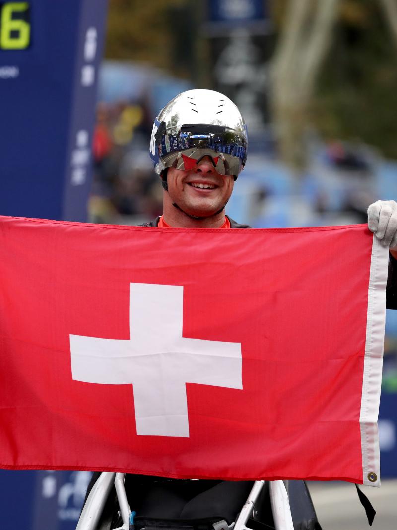 a male wheelchair racer holds up the Swiss flag