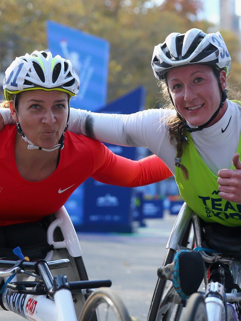 two female wheelchair racers arm in arm at the finish line