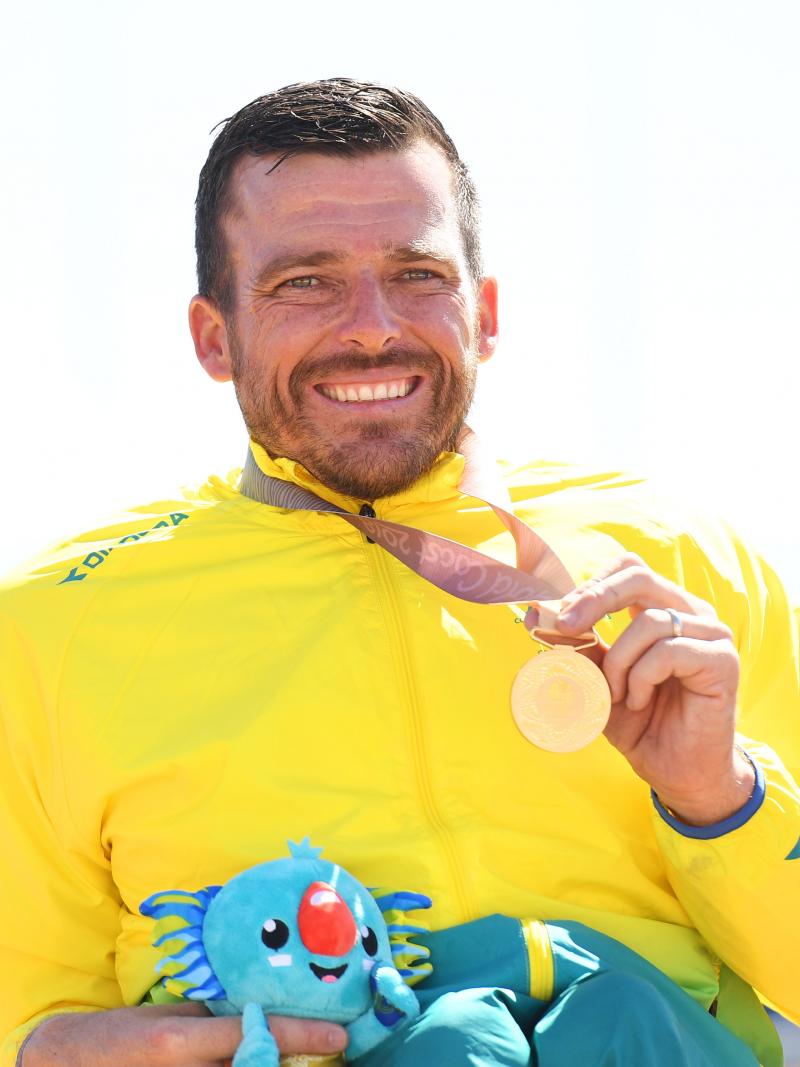 a male wheelchair racer holds up a gold medal
