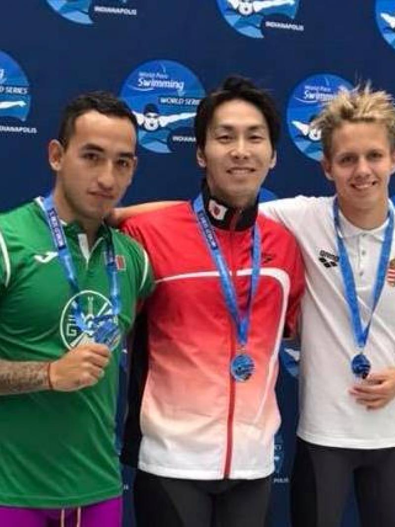 Three swimmers posing in front of a banner