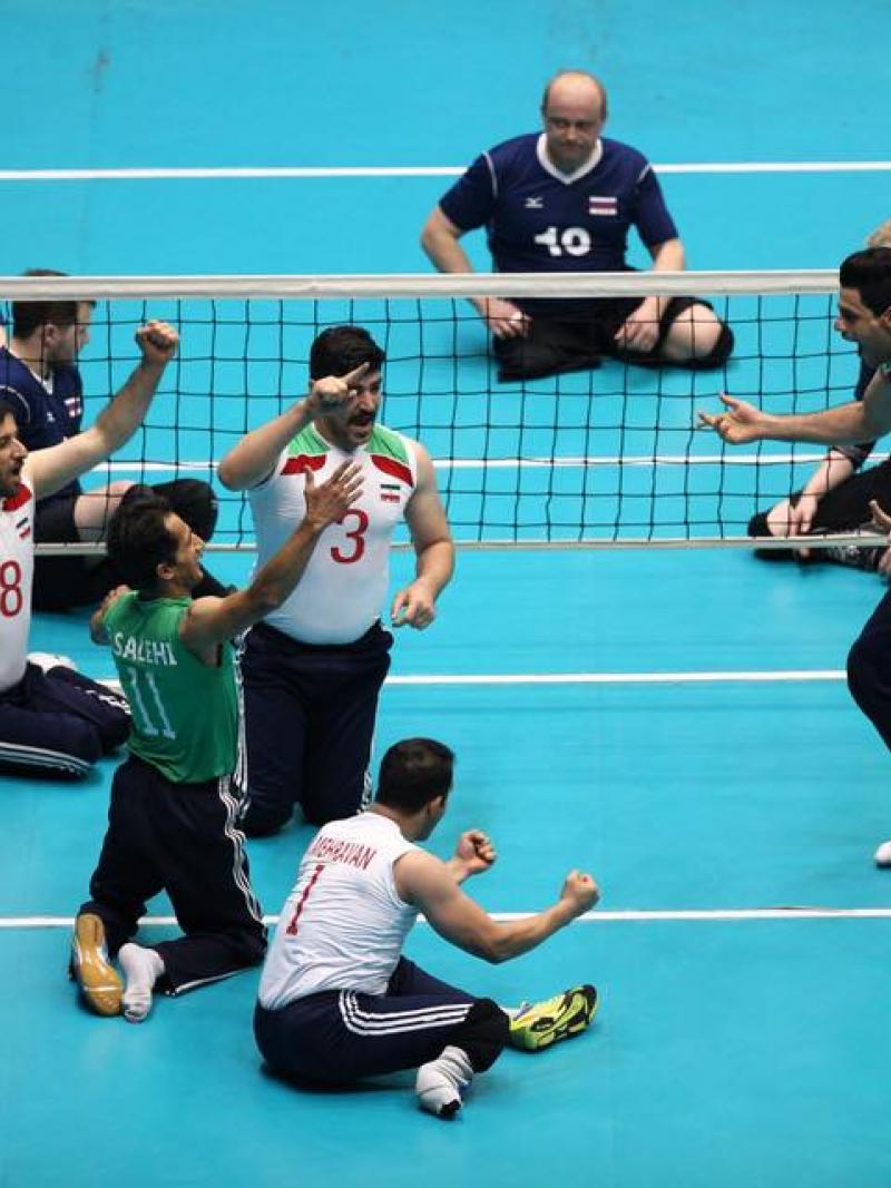 a group of male sitting volleyball players celebrate on the court