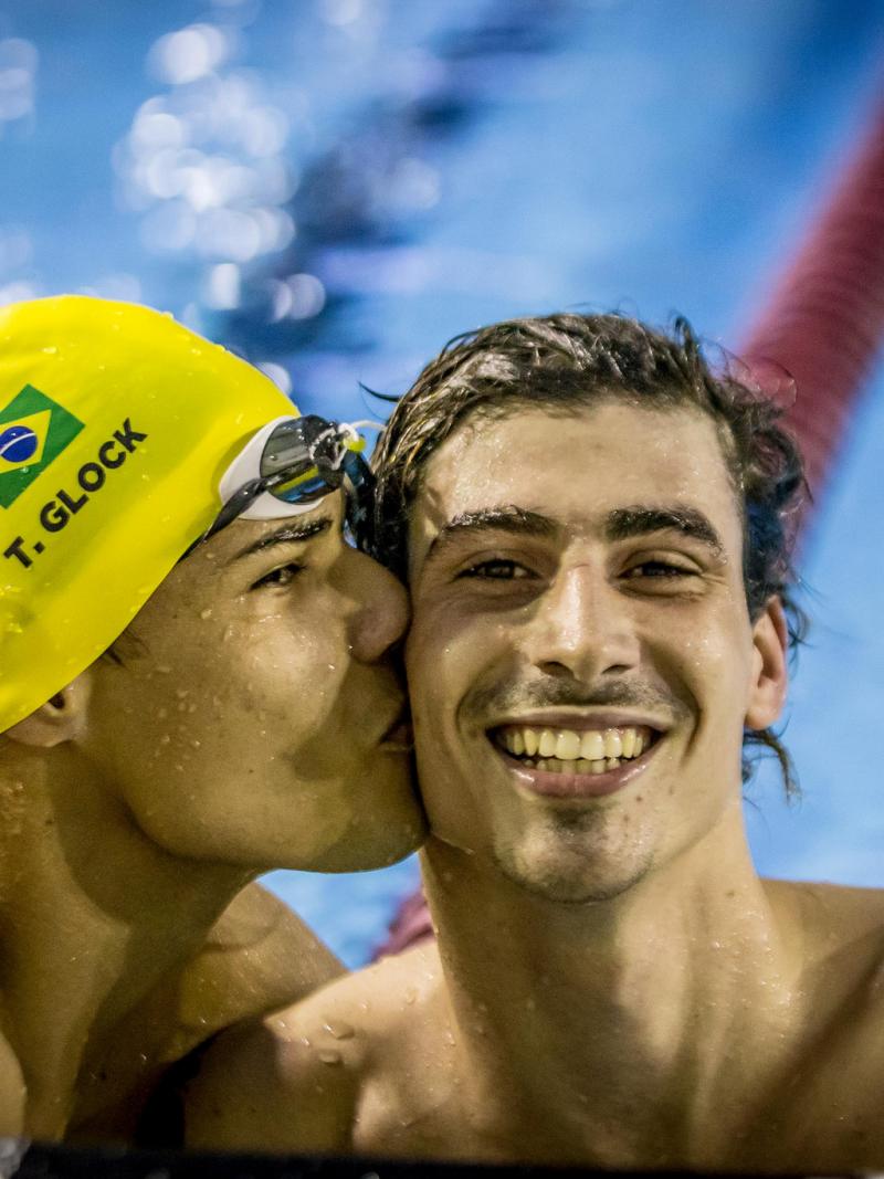 one male swimmer kissing another on the cheek in celebration