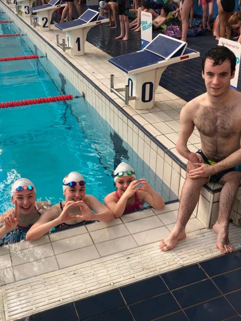 Three swimmers in the pool and one swimmer out of the pool posing for a picture
