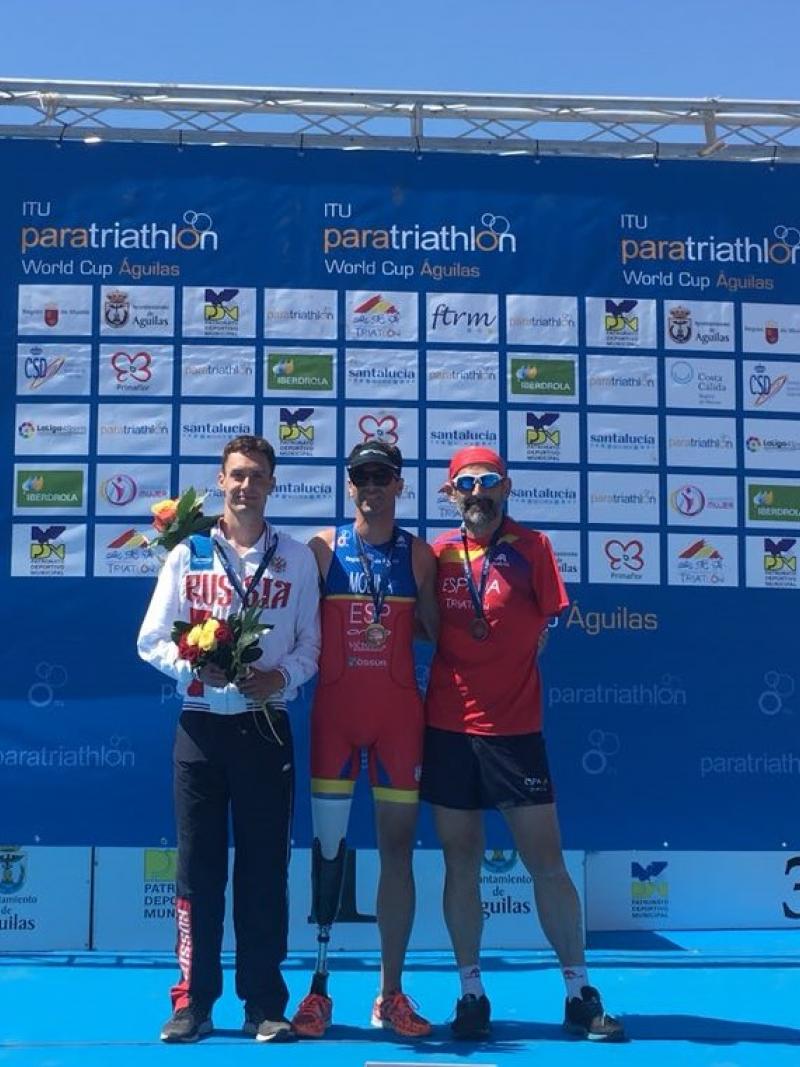 three male Para triathletes on a podium on the beach