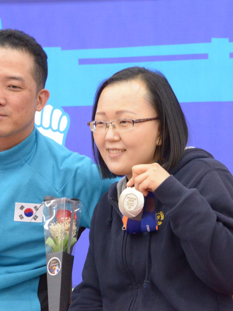 Man and woman in wheelchairs pose for photo with silver medal