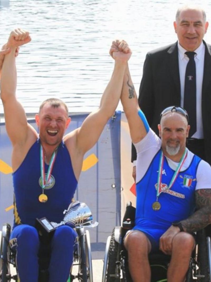 Four persons in wheelchairs and a person behind standing them