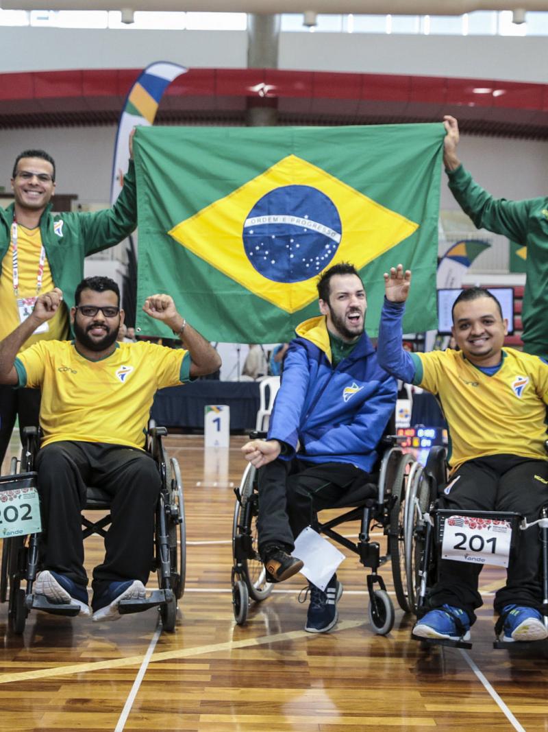 a group of boccia players wave their arms and hold up a Brazil flag