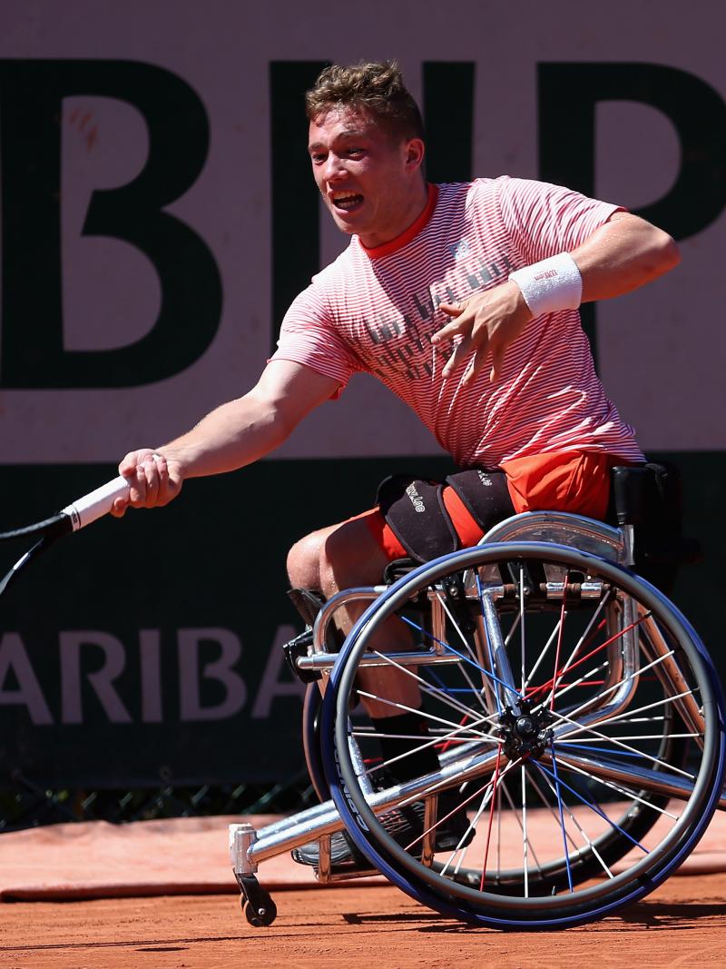 a male wheelchair tennis player reaches for a shot on a clay court