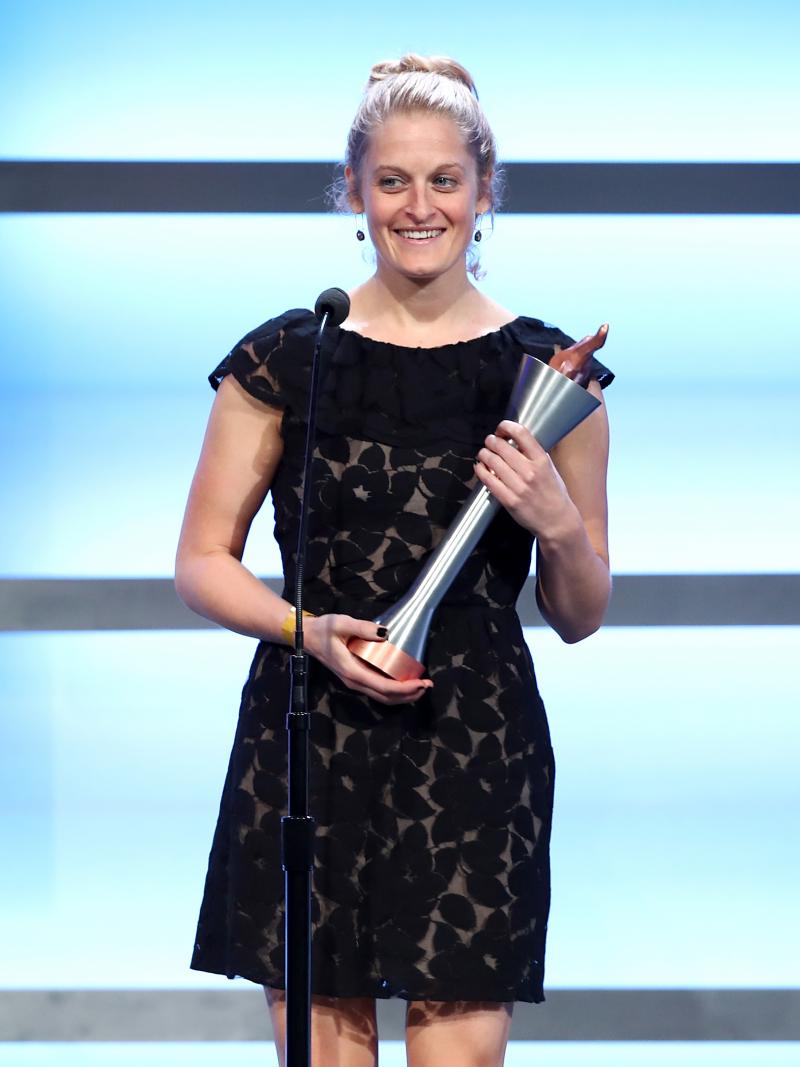 a woman stands on stage holding a trophy