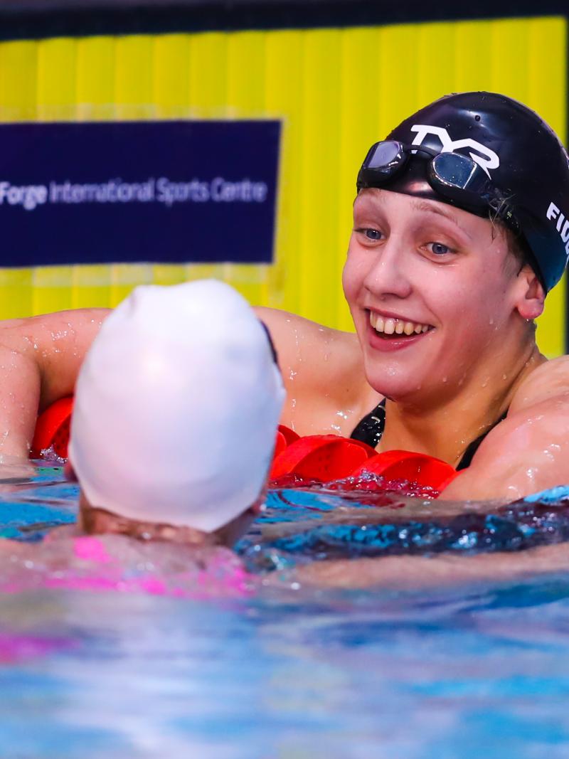 a female Para swimmer leans on the rope and chats to another swimmer