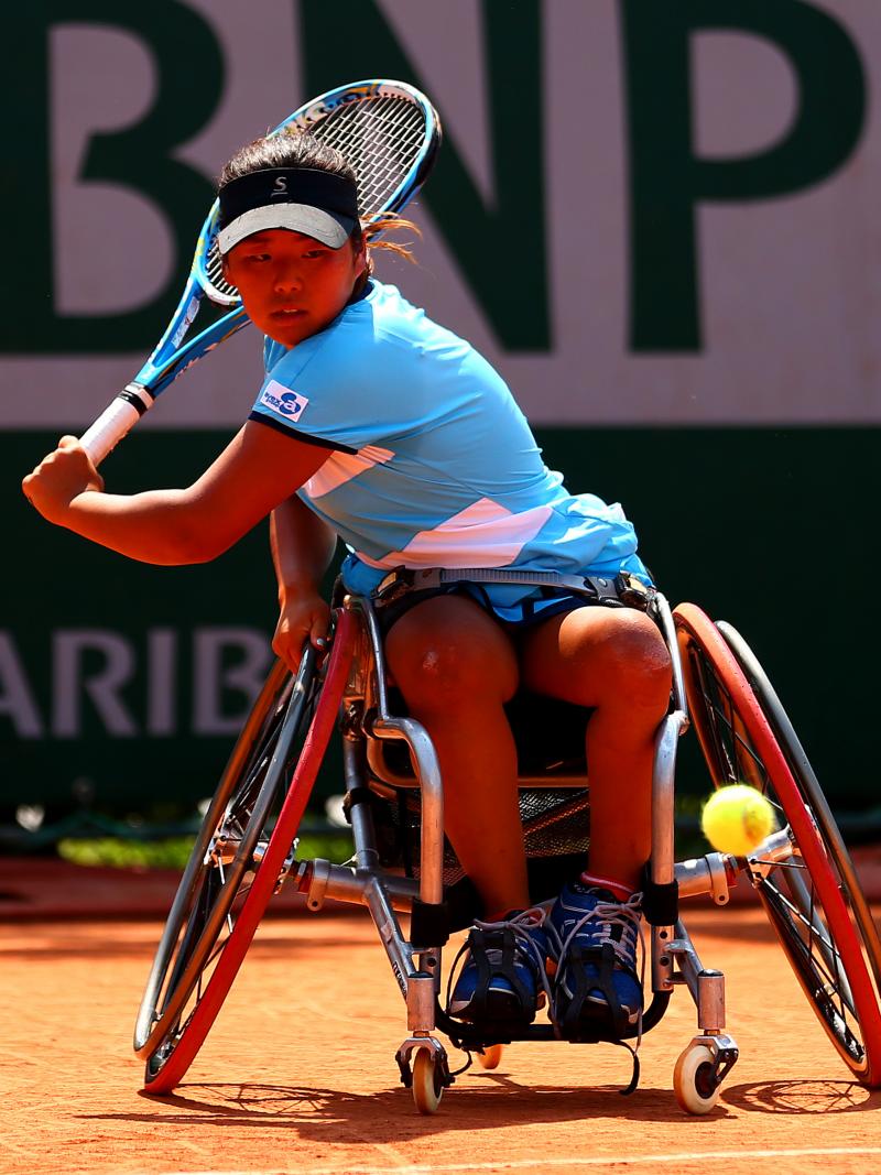 a female wheelchair tennis player plays a backhand shot