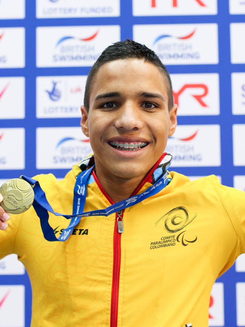 a male Para swimmer holds up his gold medal and smiles