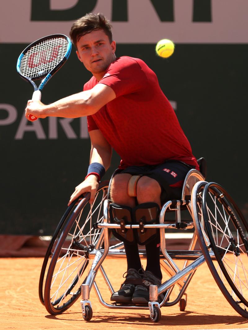a male wheelchair tennis player plays a backhand on a clay court