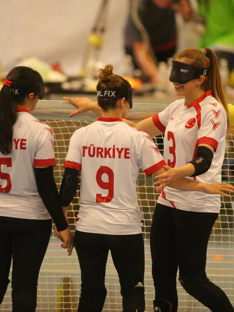 three female goalball players hug in celebration in front of the goal