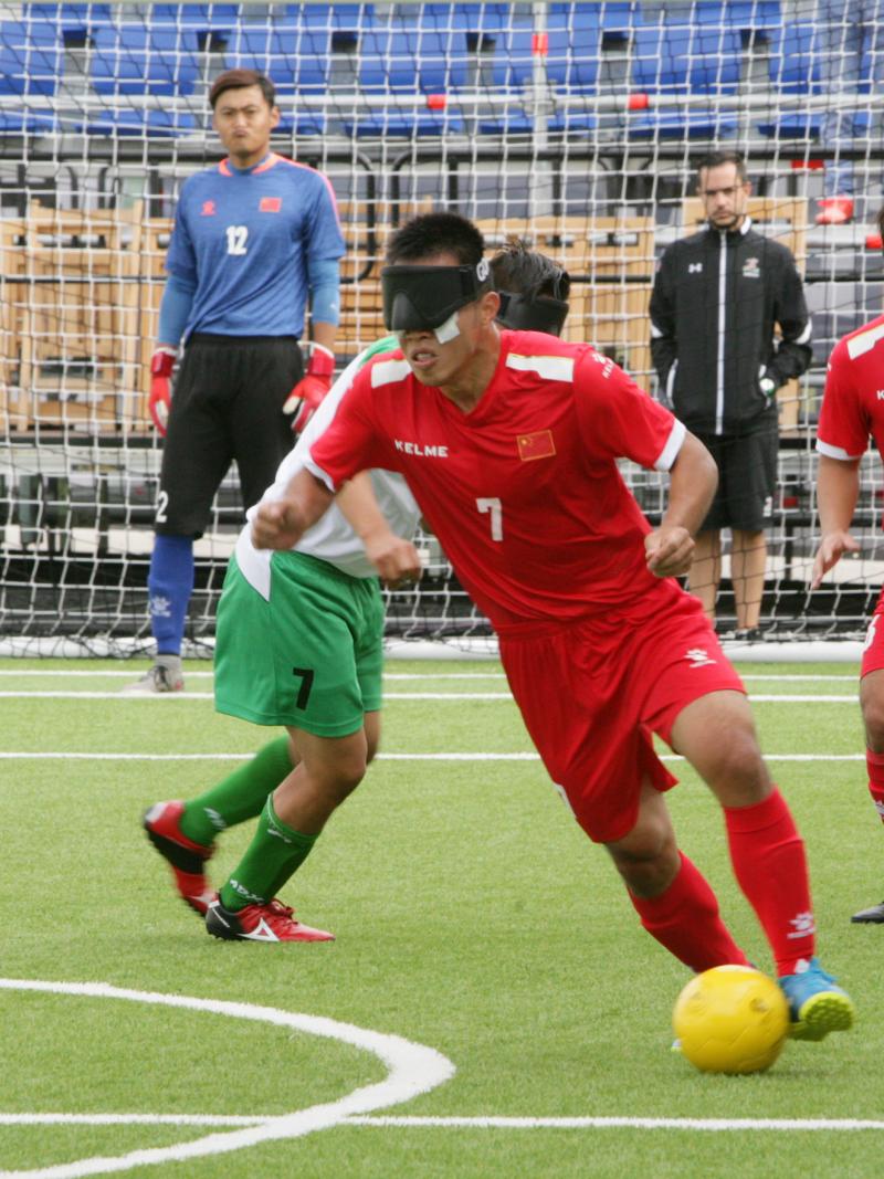 A male blind footballer dribbles past another player